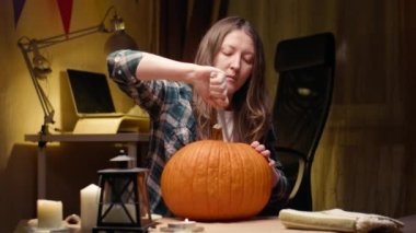 Cutting into pumpkin and taking lid with seeds out. Halloween preparations. Woman sitting and carving with knife halloween Jack O Lantern pumpkin at home for her family.