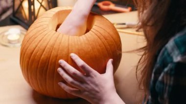 Preparing pumpkin for Halloween. Scooping out guts and seeds with spoon. Woman sitting and carving halloween Jack O Lantern pumpkin at home for her family.