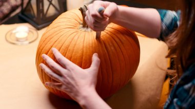 Preparing pumpkin for Halloween. Woman sitting and carving with knife halloween Jack O Lantern pumpkin at home for her family.