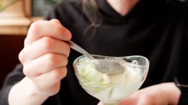 Eating vegan ice cream in cafe. Young woman with a spoon savouring dairy-free soy vanilla ice cream from sundae glass cup made of plant milk. Handheld close up shot