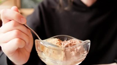 Eating ice cream in cafe. Young woman with a spoon savouring chocolate ice cream from sundae glass cup. Handheld close up shot