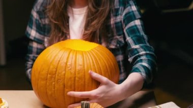 Illuminating pumpkin for Halloween. Woman sitting, lighting and showing out candle lit halloween Jack O Lantern pumpkin at home for her family.