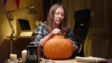 Preparing pumpkin for Halloween. Taking out lid and seeds and being grossed out by it. Woman sitting and carving halloween Jack O Lantern pumpkin at home for her family.