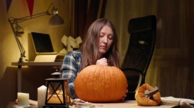 Preparing pumpkin for Halloween. Woman sitting and carving with knife face details of halloween Jack O Lantern pumpkin at home for her family.