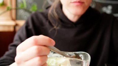 Eating ice cream in cafe. Young woman with a spoon savouring vanilla ice cream from sundae glass cup. Handheld close up shot