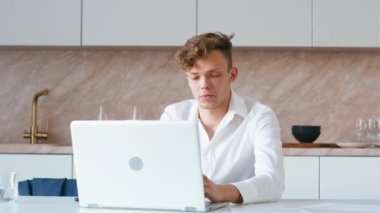 Phone call with laptop on kitchen. Young adult student receice call on smartphone and talking. Handheld shot.