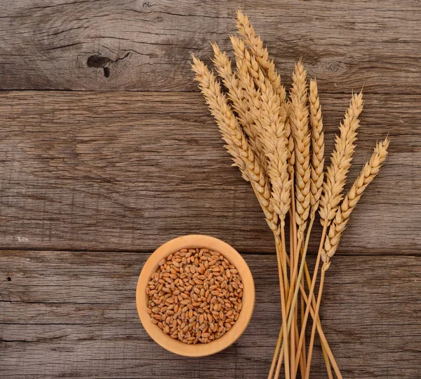 Wheat grains in a wooden bowl and wheat ears.