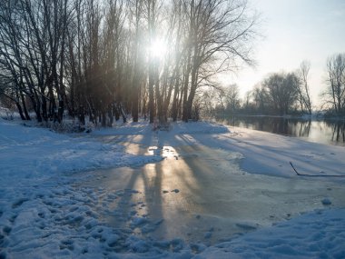Karlı kıyılar ve buzla kaplı bir kış nehrinin panoramik fotoğrafı.
