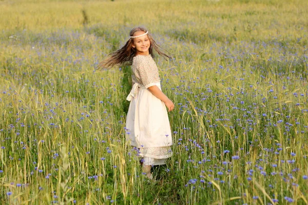 Baby girl in a long dress in the middle of the field laughing — Stock Photo, Image