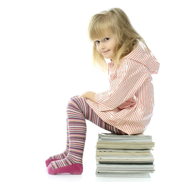 Menina sentada em uma pilha de revistas — Fotografia de Stock