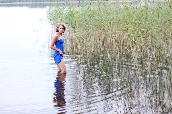 Adolescente menina em um vestido azul fica na água — Fotografia de Stock