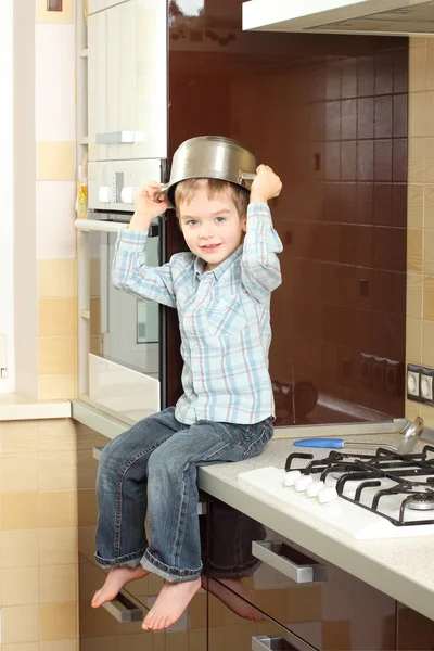 Mały chłopiec siedzi na stole z garnka na głowie — Zdjęcie stockowe