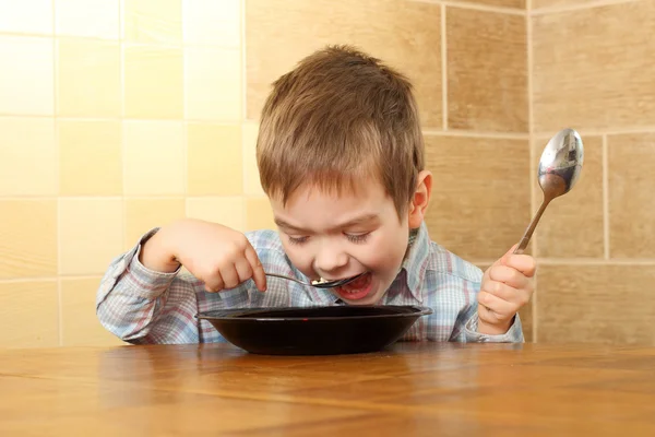 Liten pojke som äter vid ett bord med två skedar — Stockfoto