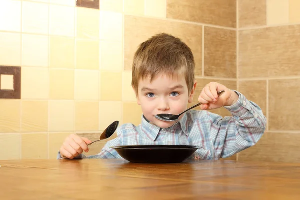 Liten pojke som äter vid ett bord med två skedar — Stockfoto