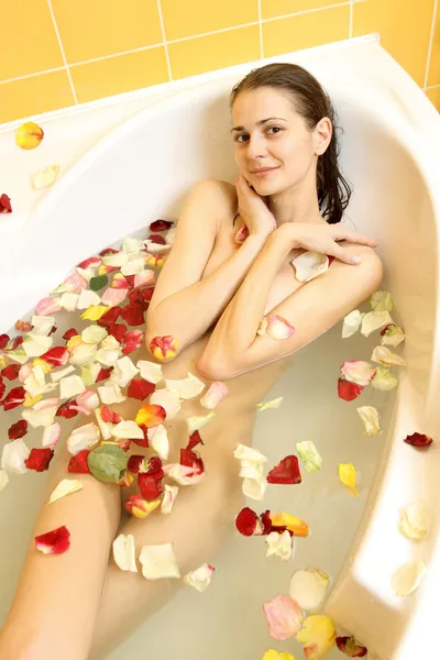 Gül yaprakları ile bir banyo içinde yatan çıplak çekici kız — Stok fotoğraf