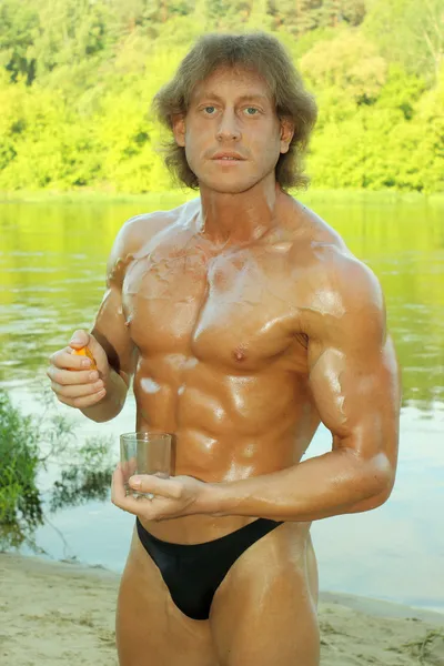 Samec fitness model kulturista vytlačuje pomerančového džusu ve sklenici — Stock fotografie