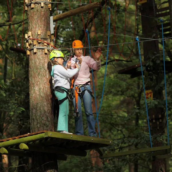 Mãe e filha em equipamentos de escalada para superar obstáculos entre árvores altas — Fotografia de Stock
