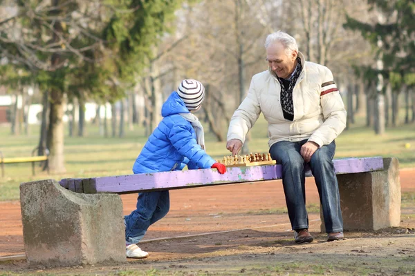 Grandfather and grandson playing chess on a bench outdoors — Stock Photo, Image