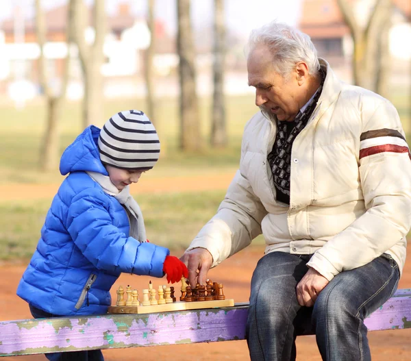 Abuelo y nieto jugando ajedrez en un banco al aire libre — Foto de Stock