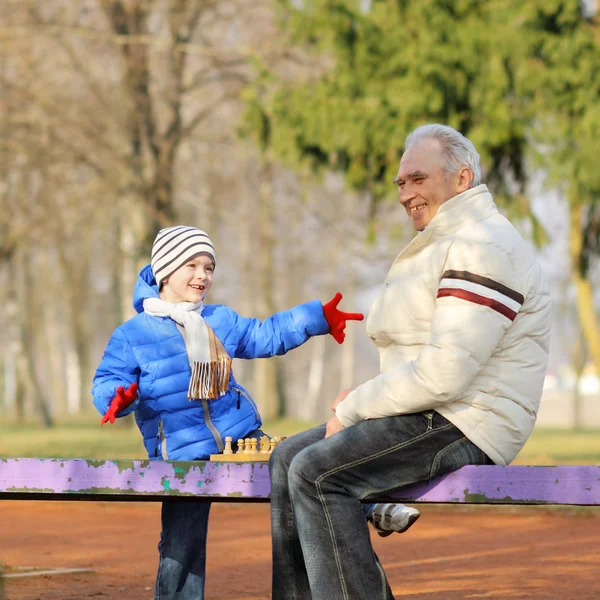 Дедушка и внук играют в шахматы на скамейке под открытым небом — стоковое фото
