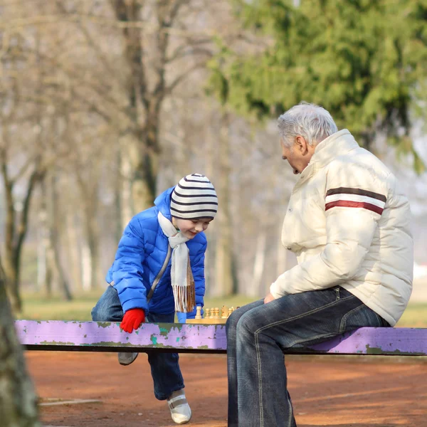 Grandfather and grandson playing chess on a bench outdoors — Stock Photo, Image