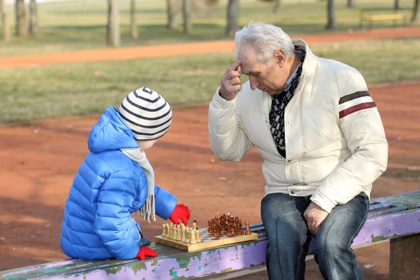 Großvater und Enkel spielen Schach auf einer Bank im Freien — Stockfoto