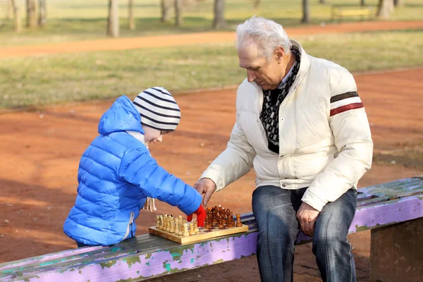 Дедушка и внук играют в шахматы на скамейке под открытым небом — стоковое фото
