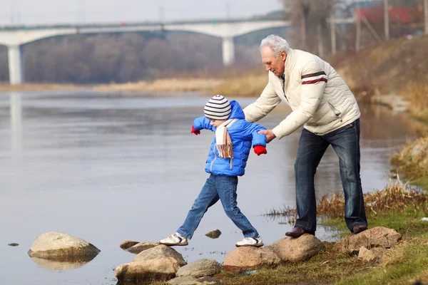 Grandfather and grandson on stones near the water — Stock Photo, Image