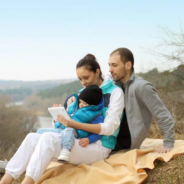 Belle jeune famille allongée sur une couverture et regardant la tablette — Photo