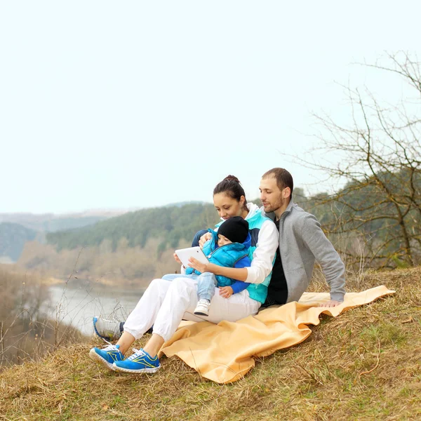 Belle jeune famille allongée sur une couverture et regardant la tablette — Photo