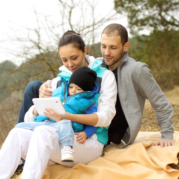 Hermosa familia joven acostada en una manta y mirando a la tableta — Foto de Stock