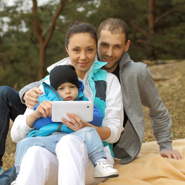 Beautiful young family lying on a blanket and looking at tablet — Stock Photo, Image