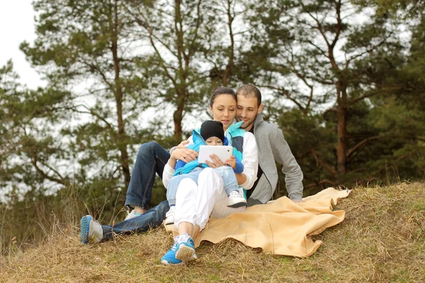 Hermosa familia joven acostada en una manta y mirando a la tableta —  Fotos de Stock