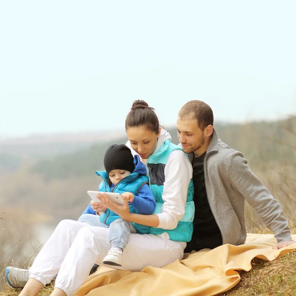 Mooie jonge familie liggend op een deken en kijken naar Tablet PC — Stockfoto