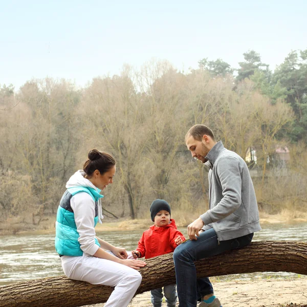 नदीजवळ एका झाडावर बसलेला तरुण कुटुंब — स्टॉक फोटो, इमेज
