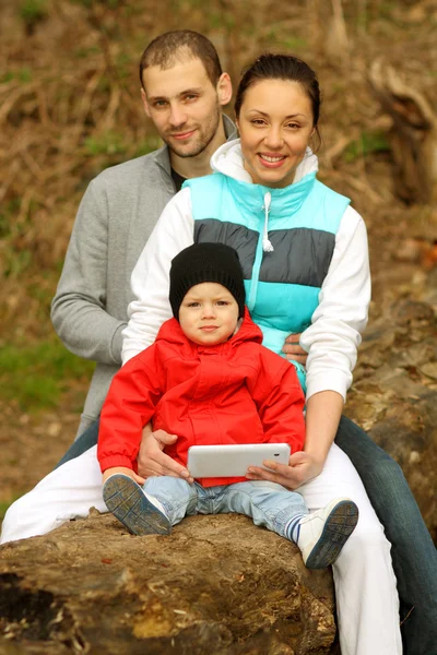 Giovane famiglia seduta su un grande albero e utilizza il tablet — Foto Stock