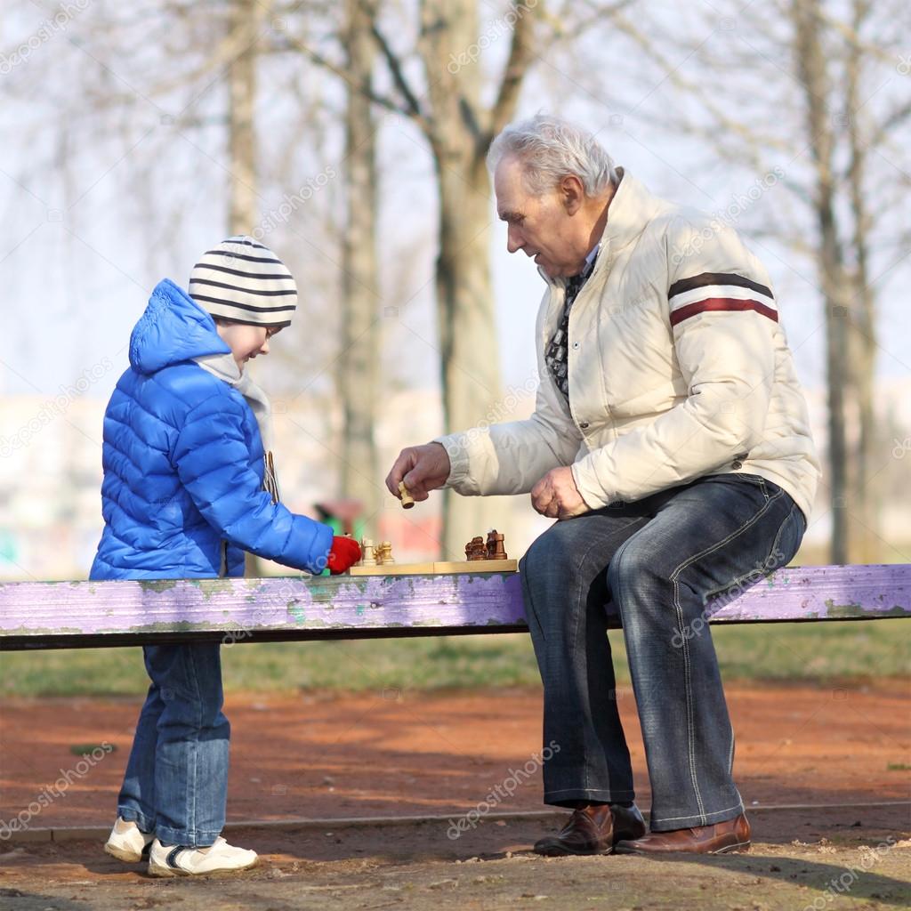 Grandfather and grandson playing chess on a bench outdoors