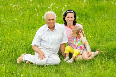 Üç yeşil çimenlerin üzerine oturan aile