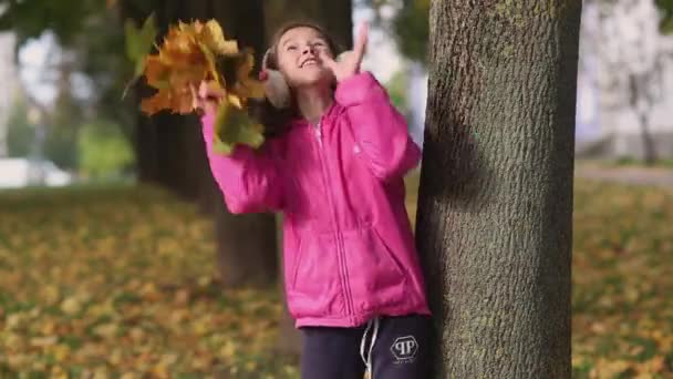 公園では秋に葉と遊ぶ幸せな女の子。木から色の葉が落ちている。. — ストック動画