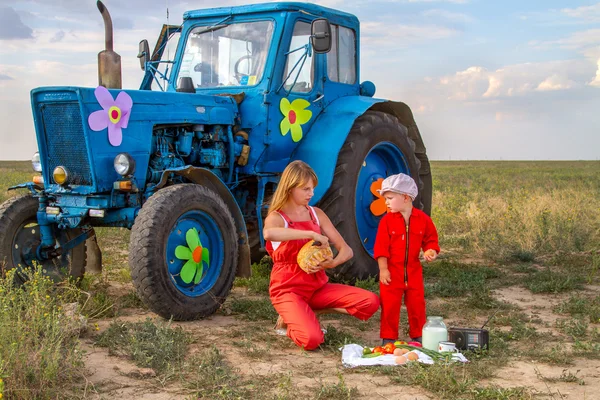 Mãe alimentando seu filho trator em um campo perto do trator — Fotografia de Stock