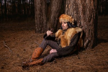 Ormandaki tilki kürkü şapkalı genç bir adamın resmi.