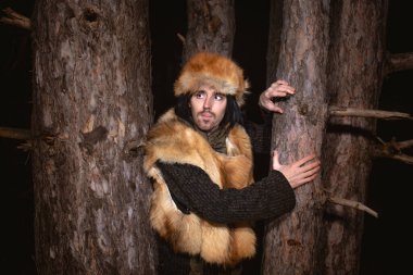 Ormandaki tilki kürkü şapkalı genç bir adamın resmi.