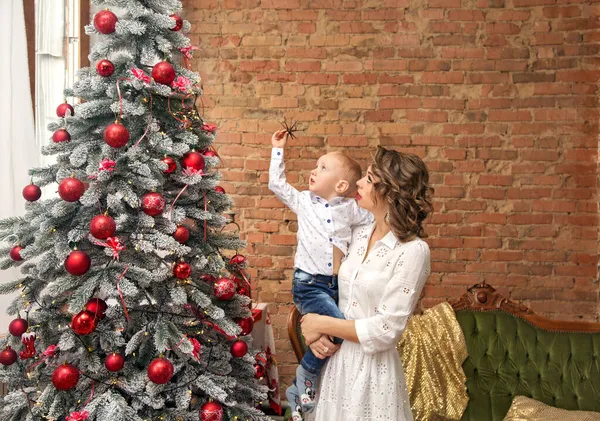 Noel ağacının yanında kucağında küçük bir oğlu olan bir annenin resmi.