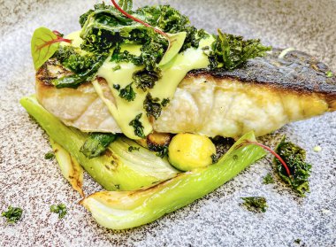 Sıcak seramik tabakta kremalı bitki sosunun altında Akdeniz usulü sotelenmiş rezene ile kızarmış deniz kabuğu.