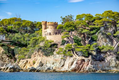 Akdeniz kıyısındaki Lloret de Mar, Costa Brava, İspanya 'da Sant Joan şatosu ve kozalaklı ağaçlarla dolu güzel kayalar.