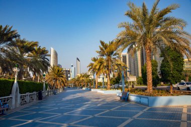 Birleşik Arap Emirlikleri 'nin başkenti Abu Dabi' deki La Corniche gezinti alanında palmiye ağaçlarından oluşan yeşil bir parkla çevrili gökdelenler..