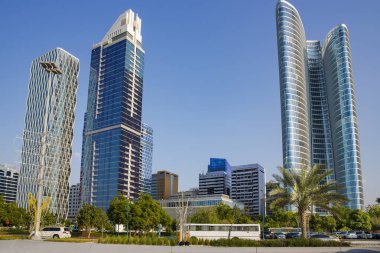 BAE, ABU DHABI, NOVEMBER, 2021 - Birleşik Arap Emirlikleri 'nin başkenti Abu Dabi' deki La Corniche gezinti alanı yakınlarında yeşil palmiye ağaçlarıyla çevrili gökdelenmiş gökdelenler.