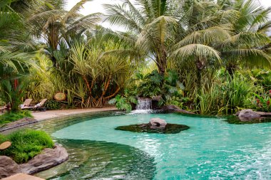 Sıcak termal suyla çevrili bir havuz bir otelin tropikal bahçesiyle The Springs Resort ve Spa 'da. Kosta Rika, Orta Amerika 'daki muhteşem Arenal Volkanı manzaralı lüks bir otel.
