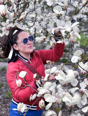 Kırmızı ceketli tatlı bir kadın, çiçek açan Magnolia stellata Royal Star ya da Star Magnolia 'nın dallarının yanında duruyor. Bahar mevsimi, tatlı koku.