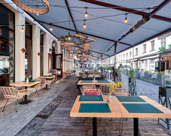 Street cafe in summer city with empty tables outdoor  in Old Town Riga, capital of Latvia. Vases of flowers on tables and cozy chairs.